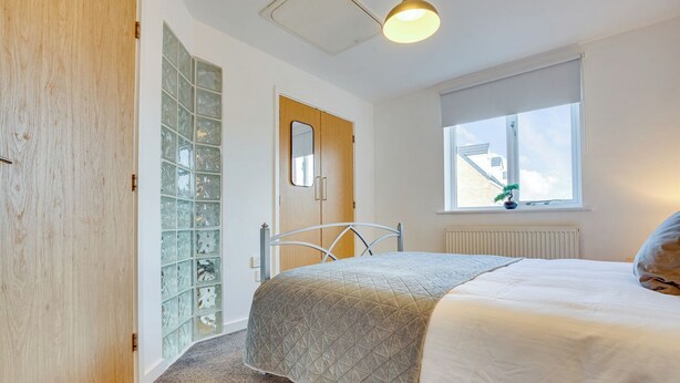 A bedroom with a bed, a window with a view, a radiator, and a door with a mirror. - Quaint 1 Bedroom 1st Floor Flat (Doncaster)