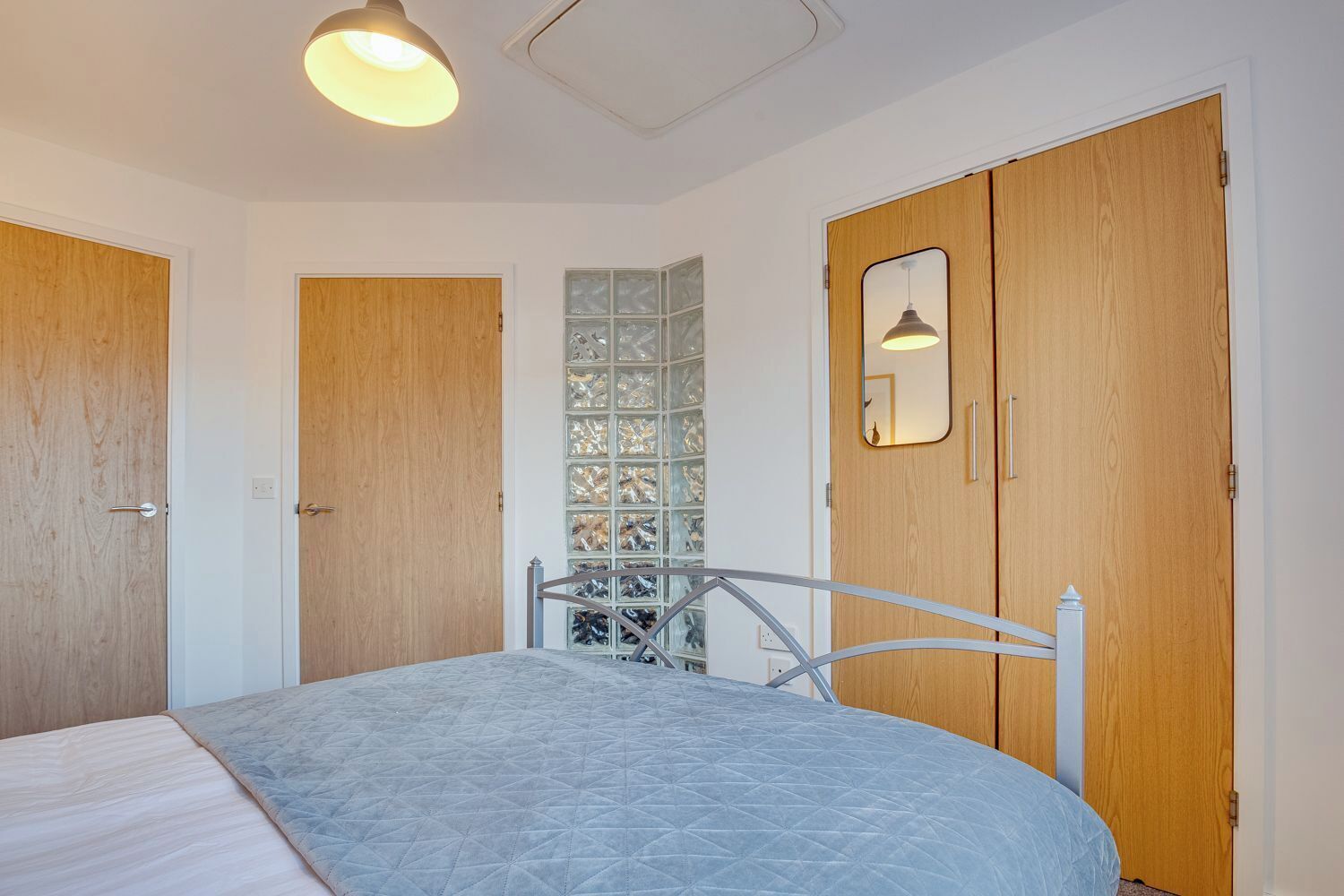 A bedroom with a bed, wooden doors, a glass partition, and a mirror.