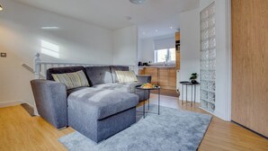 A modern living room with a grey sofa, a small side table, and a kitchen in the background. - Quaint 1 Bedroom 1st Floor Flat (Doncaster)