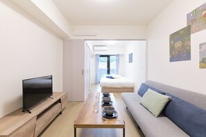 Una habitación moderna con televisor de pantalla plana, una mesa de madera con cuencos y vasos, un sofá y una cama al fondo.