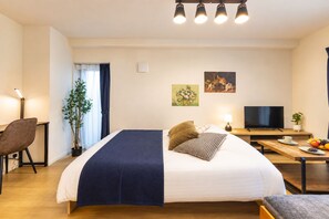 A hotel room with a bed, a desk with a TV, a chair, a plant, and artwork on the walls. - Mugenzaka by Tranova (Tokyo)