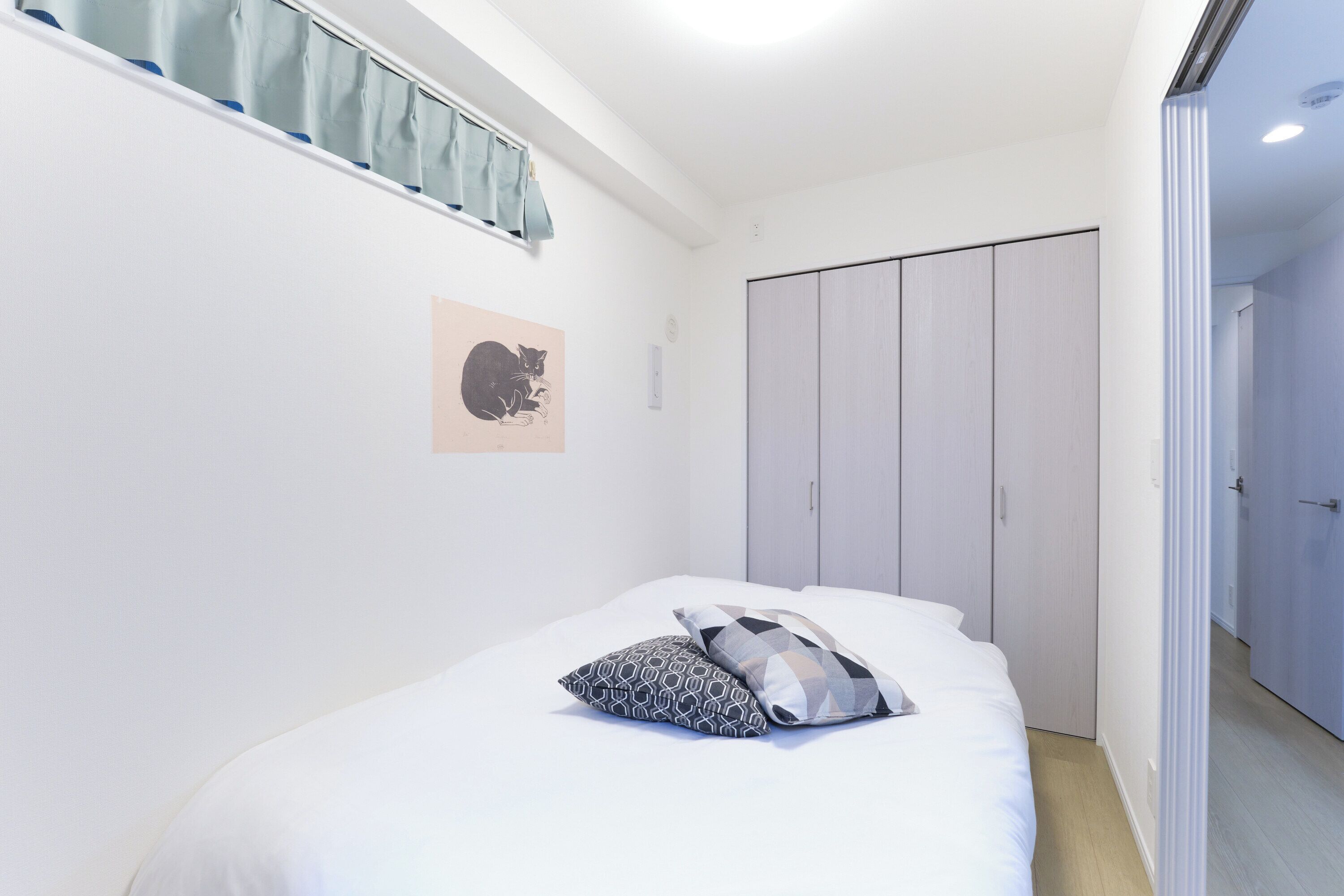 Ein Schlafzimmer mit Bett, Kleiderschrank, einem Fenster mit Vorhängen und einem Wandbild.