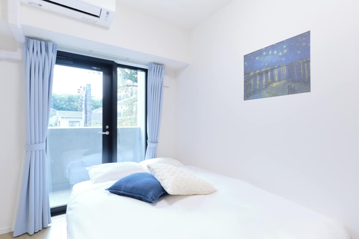 A bedroom with a bed, a window with curtains, and a painting on the wall.