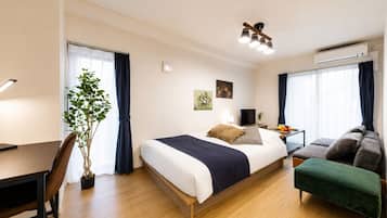A hotel room with a bed, a desk, a chair, a plant, a TV, and a sofa.