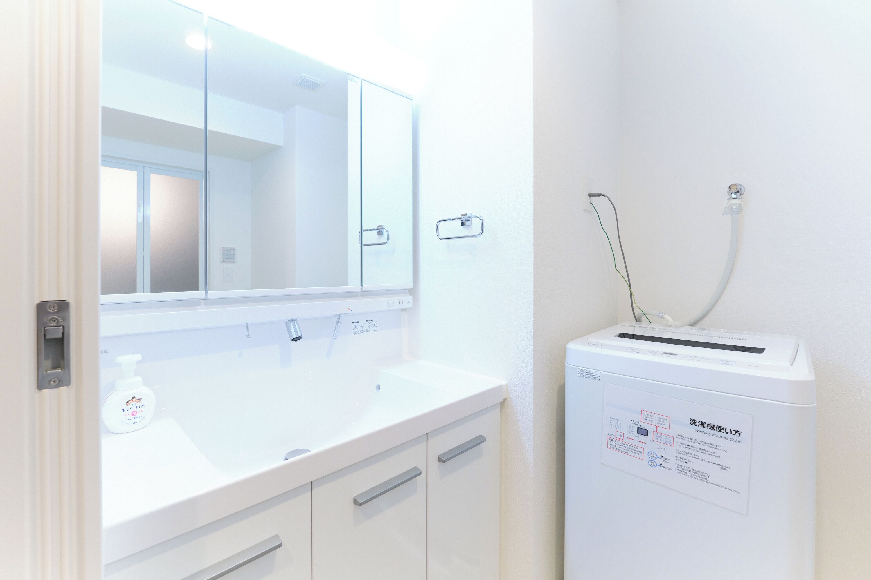 A bathroom with a white sink, mirror, and a white washing machine.