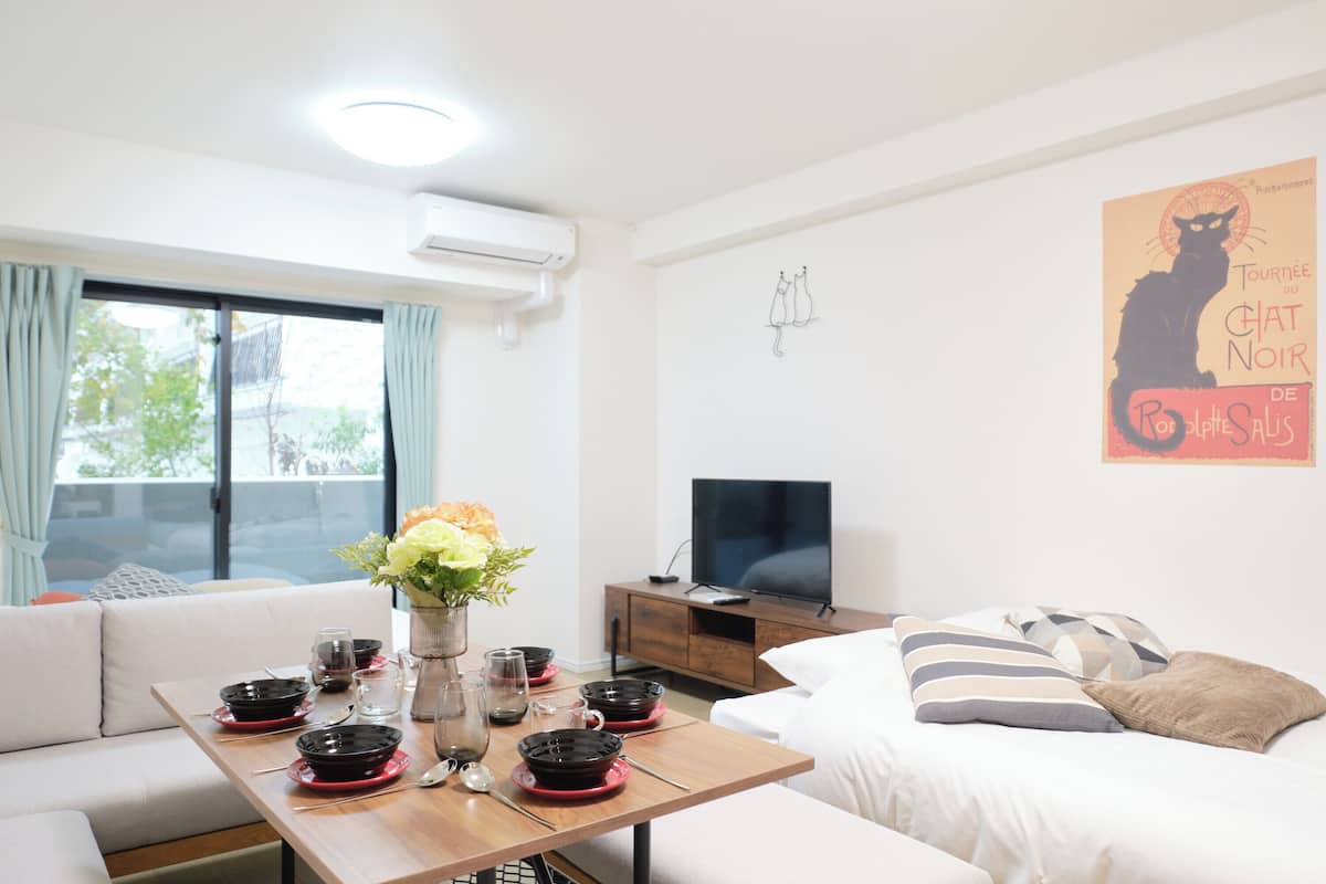 A modern room with a dining table set for four, a sofa, a TV, and a poster on the wall.