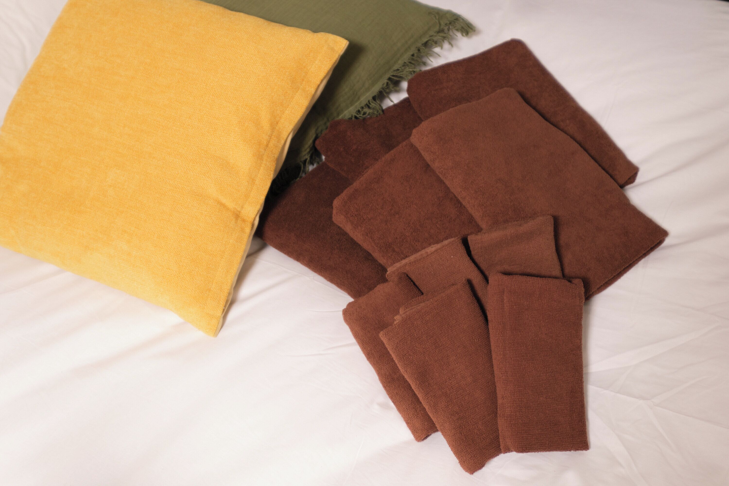 Ein Bett mit weißer Bettdecke, einem gelben Kopfkissen und mehreren braunen Handtüchern.