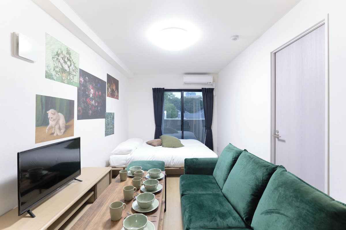 A room with a bed, green sofa, TV, and a table with cups.