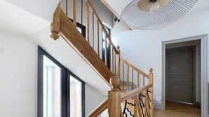 A staircase with wooden balusters and a black metal railing, leading to a room with large windows and a ceiling fan.