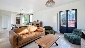 A spacious living room with a brown leather sofa, a wooden coffee table, and a green armchair. There is a dining area in the background with a wooden table and chairs.