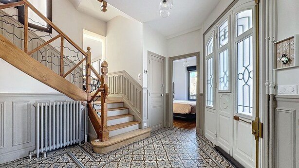 A hallway with patterned floor tiles, a wooden staircase, and a door with a brass handle.