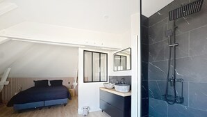 A bedroom with a bed, bedside table, and a bathroom with a shower and sink.