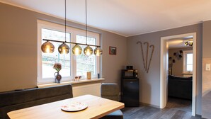 Una cocina moderna con una mesa de comedor, asientos tipo banco, iluminación colgante y un refrigerador.