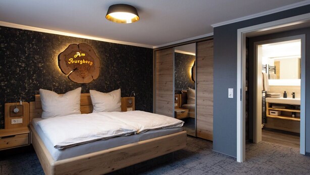 Un dormitorio moderno con una cama de madera, un reloj de pared redondo y un espejo en la habitación contigua.