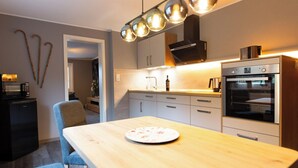 Una cocina moderna con una mesa de madera, horno empotrado e iluminación colgante.