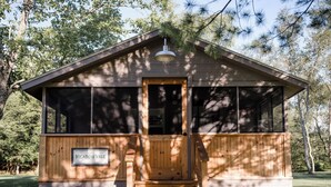 Une cabane en bois dotée d’un porche, portant l’inscription « Meadow Vale », et entourée d’arbres.