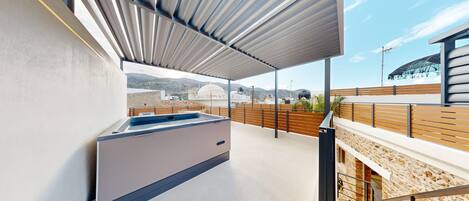 Eine Dachterrasse mit integriertem Whirlpool, Blick auf die Stadtlandschaft und einer Steinmauer.