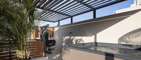 A modern outdoor area with a pergola, exercise equipment, and a large planter with a palm tree.