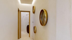 A hallway with a door leading to a bathroom, a wall-mounted towel rack, and a round, textured wall decoration.