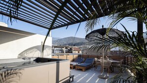En takterrass med solstolar, ett bord och en pergola som ger skugga.