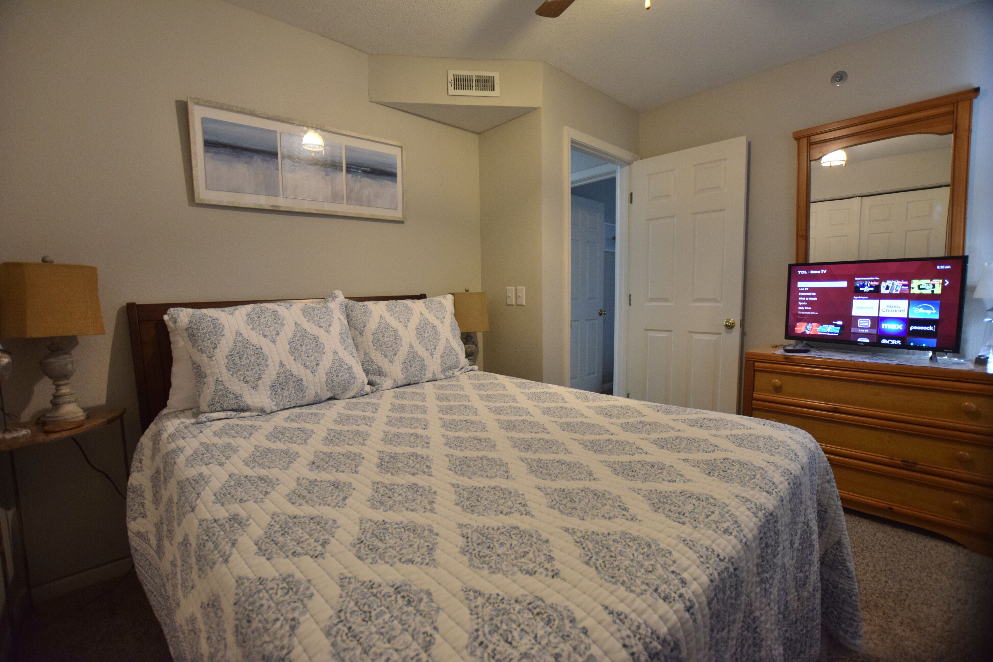 A bedroom with a bed, a dresser, a television, and a door leading to another room.