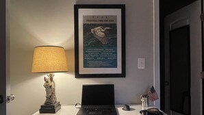 A desk with a laptop, a framed poster, a lamp, and a small American flag. - Charming 2-bedroom renovated historic home in downtown Raleigh. (Raleigh)
