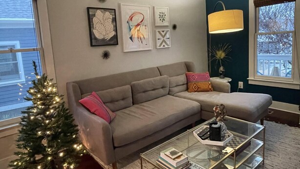A living room with a grey sectional sofa, a glass coffee table, and a small Christmas tree. - Charming 2-bedroom renovated historic home in downtown Raleigh. (Raleigh)