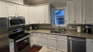 A modern kitchen with white cabinets, stainless steel appliances, granite countertops, and a window providing natural light. - Charming 2-bedroom renovated historic home in downtown Raleigh. (Raleigh)