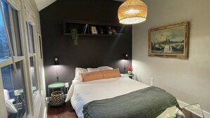 A bedroom with a bed, bedside lamps, a hanging light fixture, a painting, and a shelf with books and a vase. - Charming 2-bedroom renovated historic home in downtown Raleigh. (Raleigh)