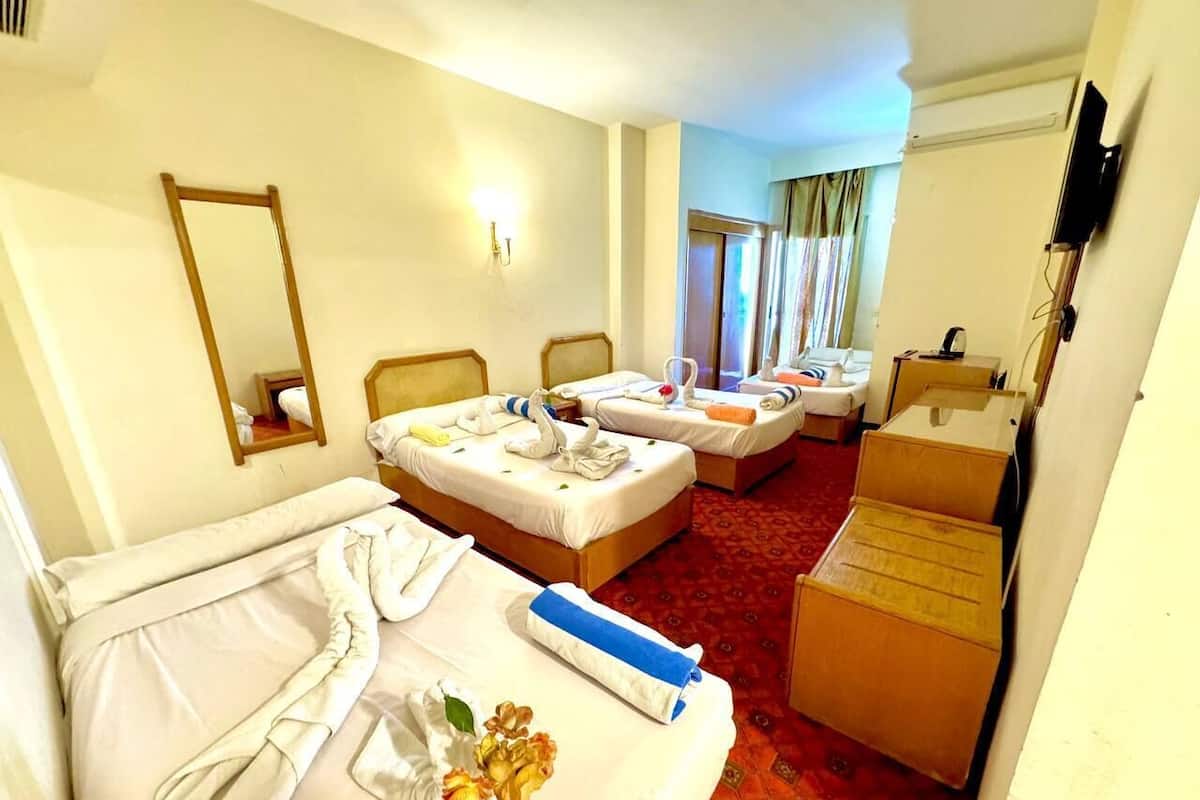 A hotel room with two beds, a mirror, a television, and a red carpet.