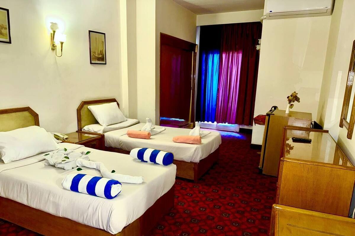 A hotel room with two beds, a wooden dresser, a desk, and a red carpeted floor.