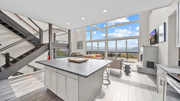 Une cuisine moderne dotée d’un grand îlot central, d’un coin repas offrant une vue agréable et d’un escalier menant à un étage supérieur.