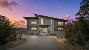 Une maison moderne à deux étages, dotée de fondations en pierre, de grandes fenêtres et d’une allée menant à l’entrée.