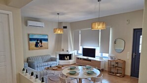 Un salon moderne avec un canapé, une table à manger et des chaises. On y trouve également un téléviseur, une cheminée et une fenêtre avec des stores.