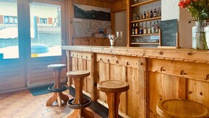 Un coin bar en bois avec des tabourets, un présentoir à bouteilles de vin et un menu écrit à la craie.