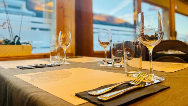 Une table mise pour le dîner, avec des verres à vin, des couverts et un menu.