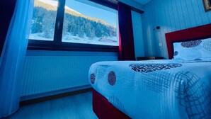 Une chambre avec une grande fenêtre, un lit recouvert d’une literie à motifs, et une vue sur un paysage enneigé.