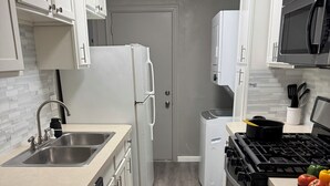 Une cuisine moderne avec des meubles blancs, un évier en acier inoxydable, un lave-vaisselle, un réfrigérateur, un four à micro-ondes et une cuisinière.