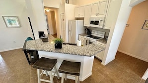 A kitchen with white cabinets, a granite countertop, two bar stools, and a built-in oven.