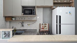 A modern kitchen with grey cabinets, a microwave, a white refrigerator, a gas stove, and a granite countertop. - Studio - Av. Presidente. Kennedy  V. Tupi - PG (Vila Tupi Praia Grande)