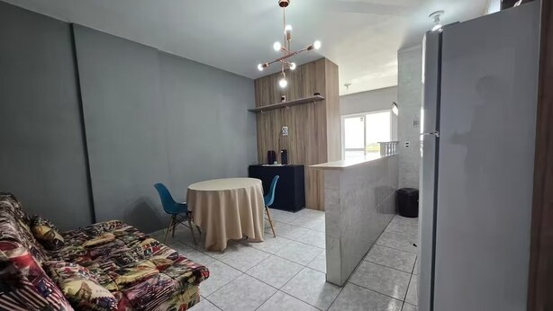 A compact living space with a sofa, a dining table, and a kitchenette area. - Studio - Av. Presidente. Kennedy  V. Tupi - PG (Vila Tupi Praia Grande)