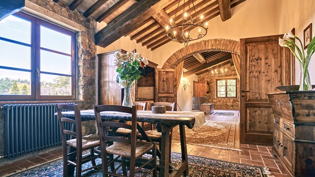 A rustic dining area with a wooden table and chairs, a chandelier, and a view through an arched doorway. - Podere La Marroneta (Tuscany Hills & private Pool) (Rivalto)