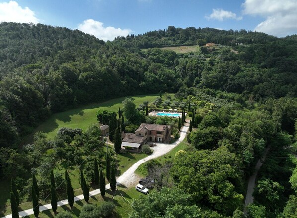 Uma casa grande com piscina, rodeada por vegetação exuberante e colinas.