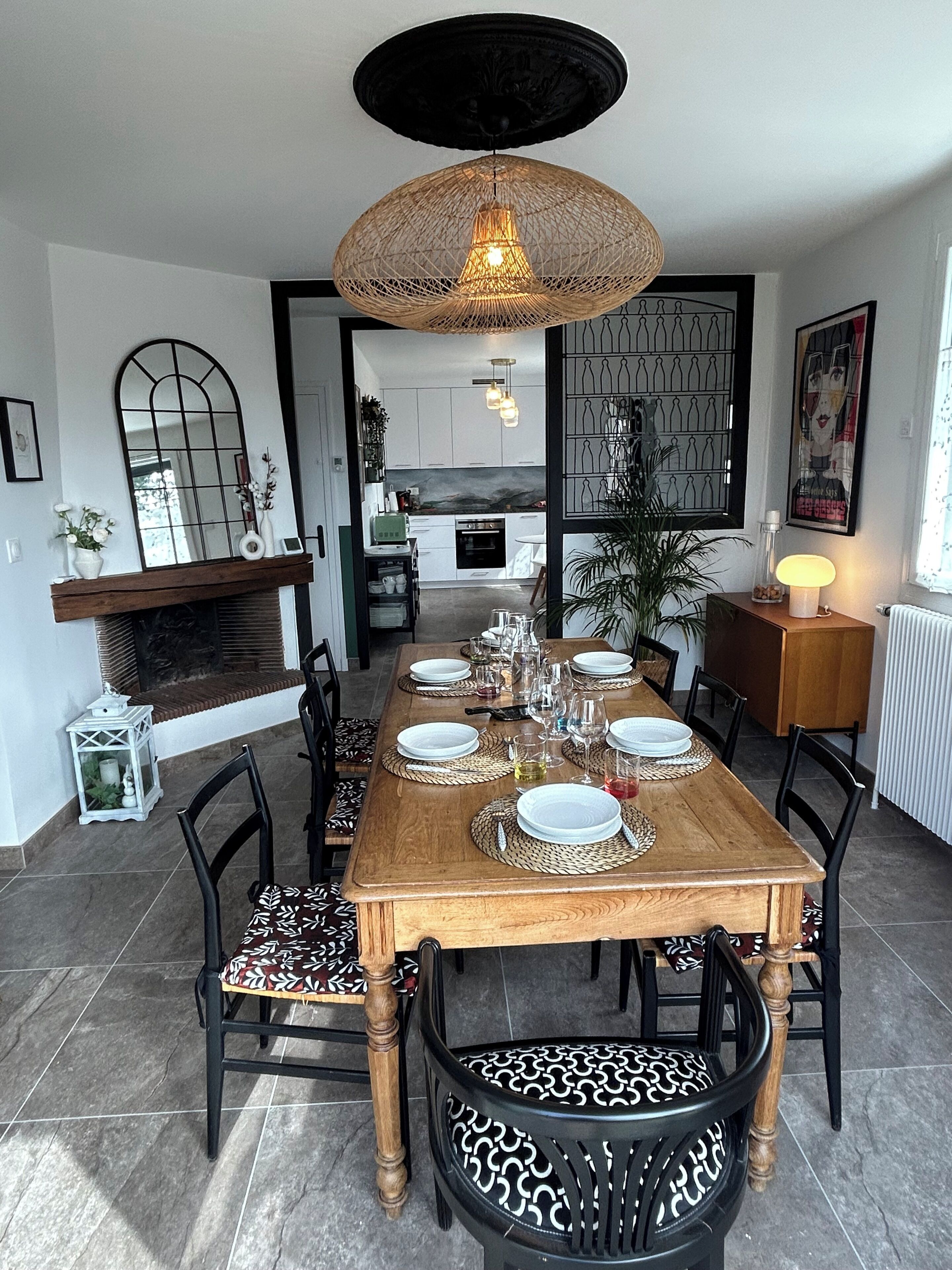 Een eetruimte met een houten tafel gedekt voor zes personen, omringd door zwarte stoelen met gestreepte kussens. Daarboven hangt een grote geweven lamp.