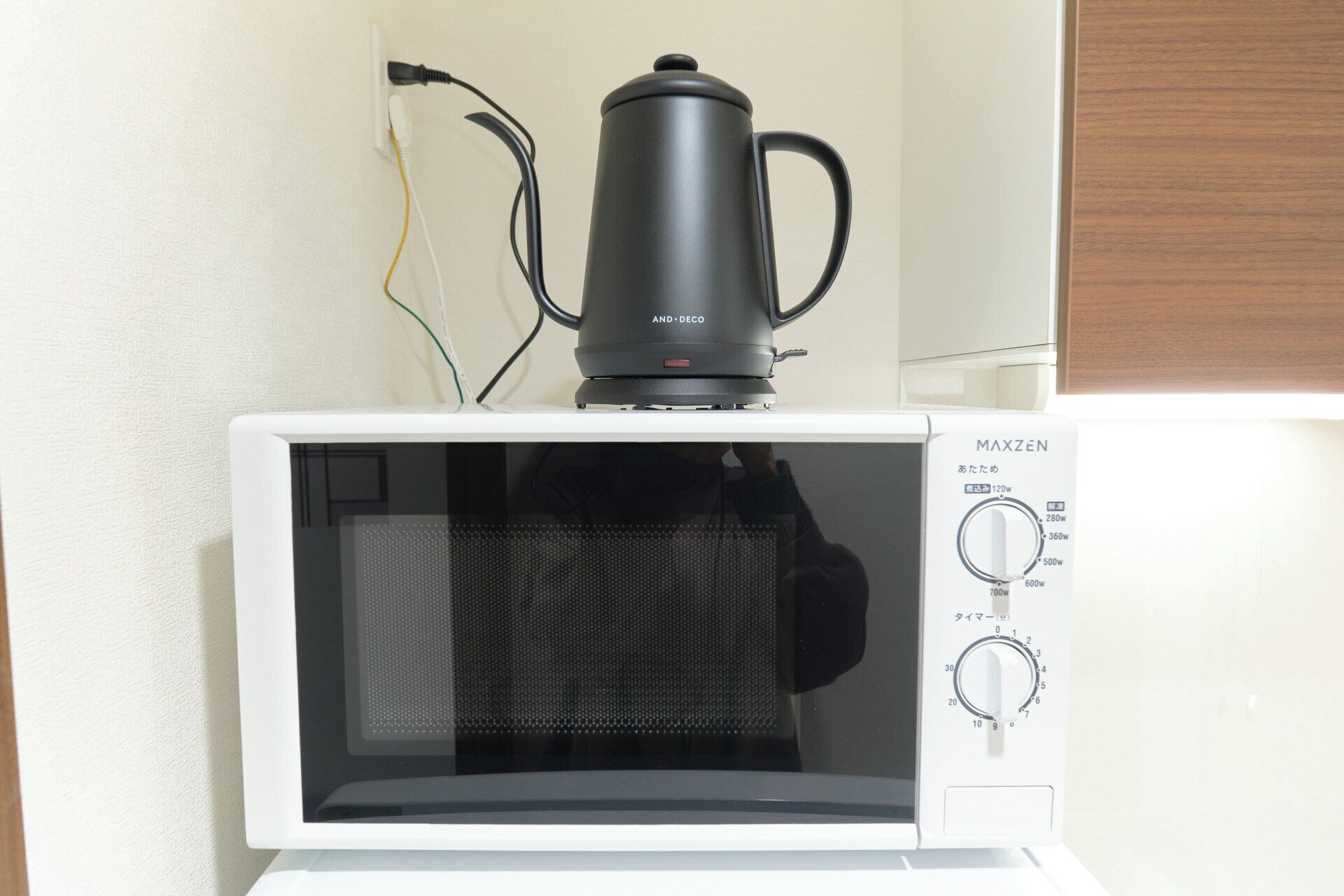 Un four à micro-ondes sur lequel est posée une cafetière noire, un panneau de commande avec des réglages de puissance, et une personne à l’arrière-plan.