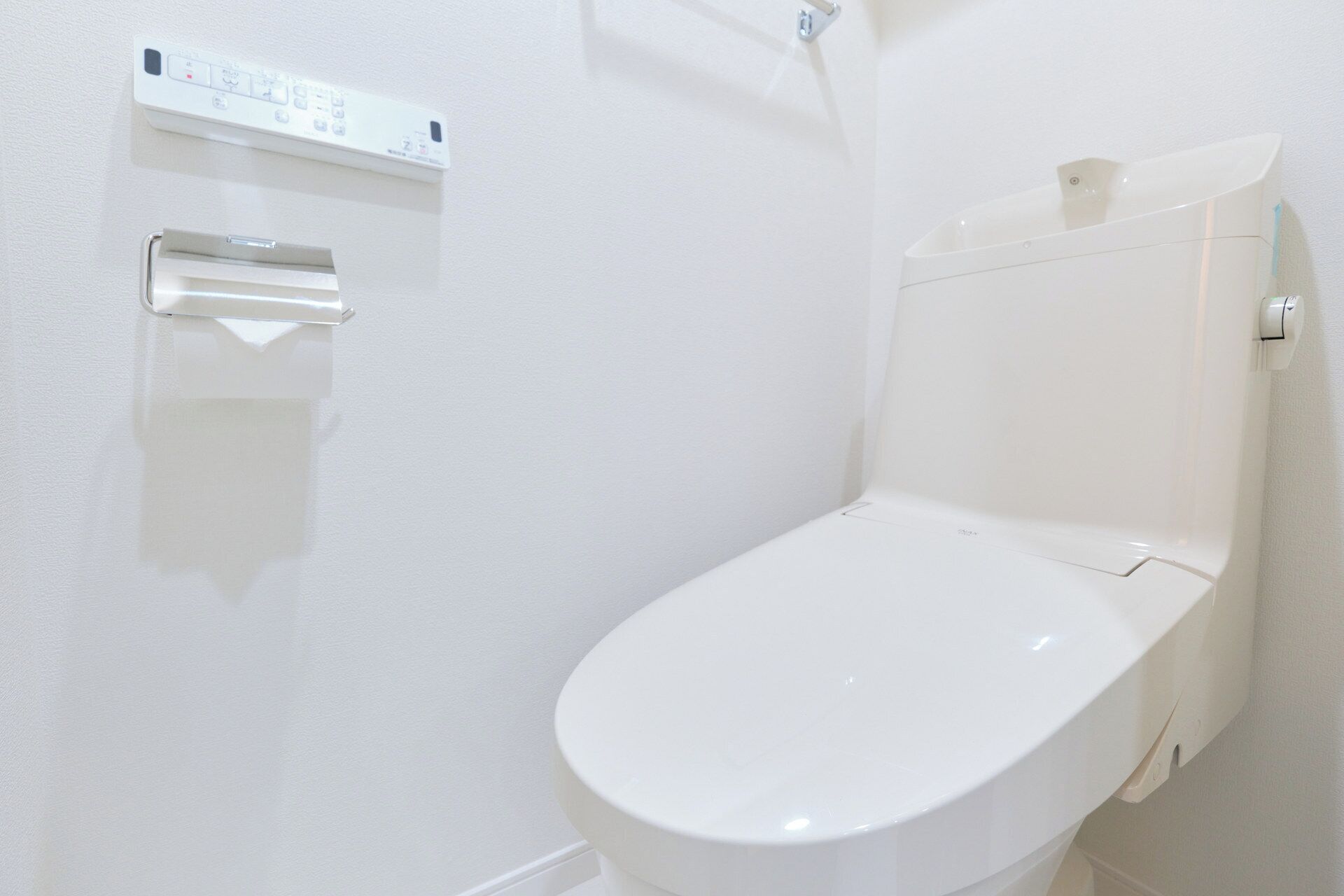 A white toilet with a flush handle and a wall-mounted flush button.