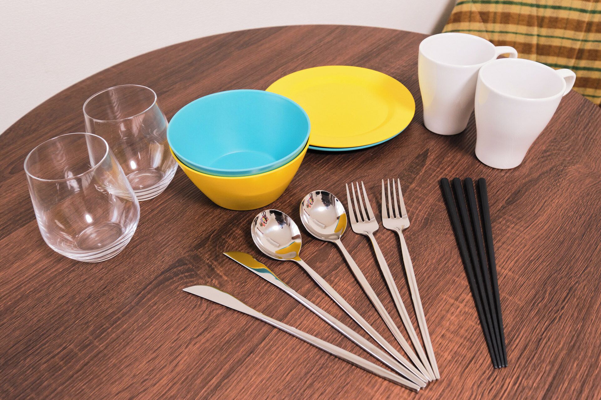 A dining table with cutlery, plates, and cups.