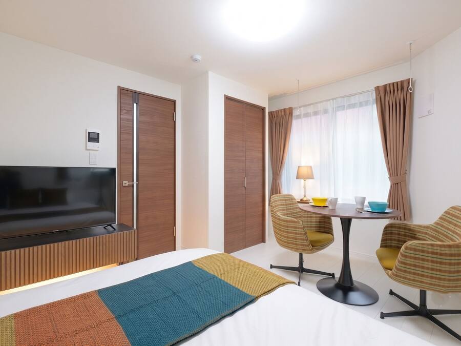 A hotel room with a bed, a TV, a desk with two chairs, and a window with curtains.