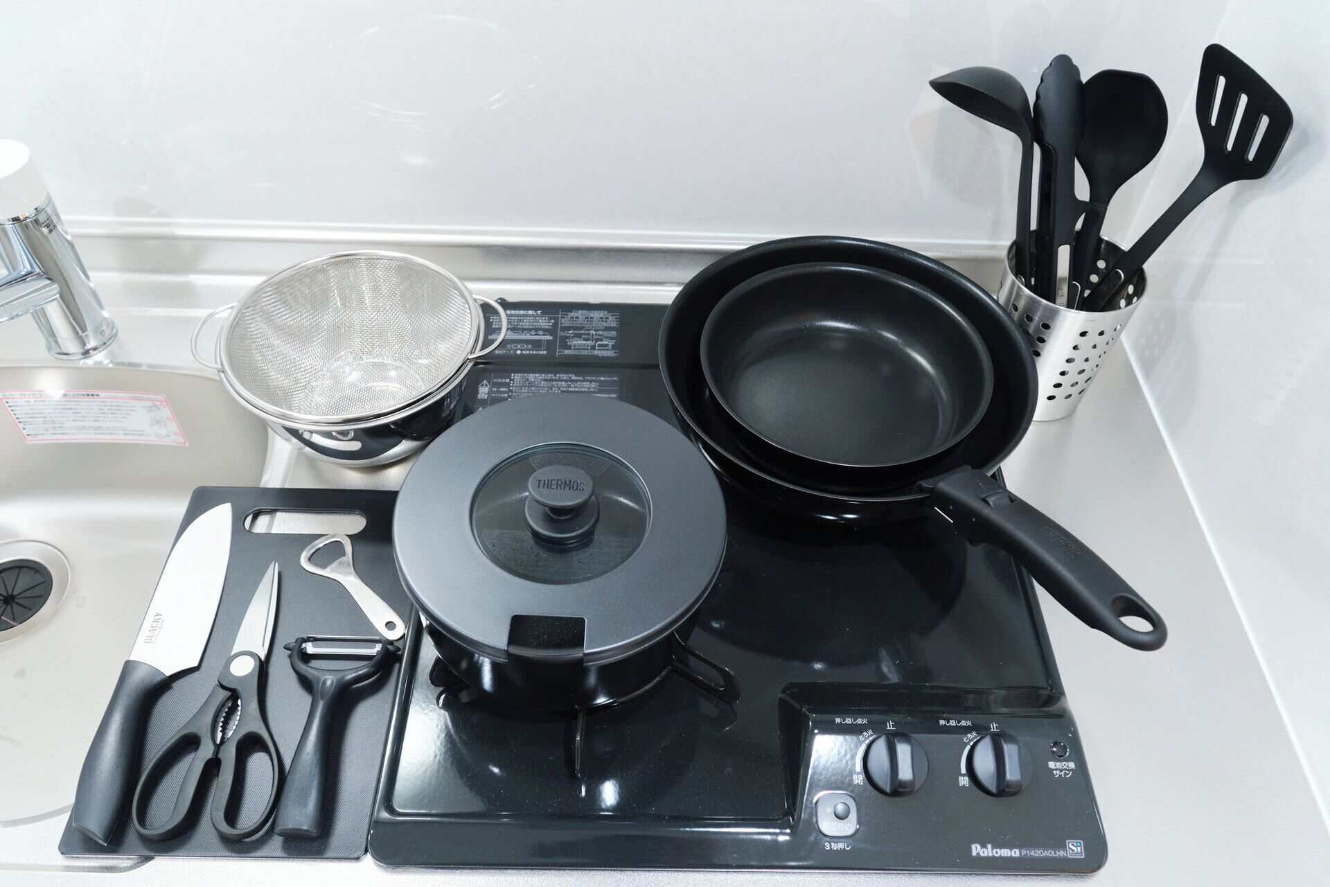 A kitchen with a stove, a pot, a strainer, a spatula holder, and a pair of scissors.