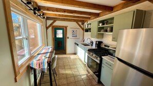 Una cocina con vigas de madera, una mesa de comedor con mantel colorido y vistas a través de una ventana.